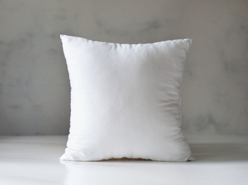 May include: A white pillow with a smooth, plain surface. The pillow is sitting on a white surface.