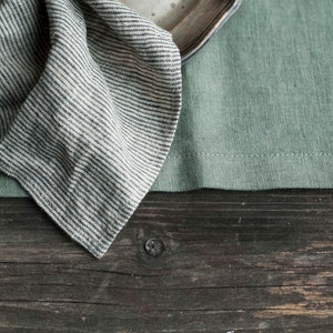 May include: A striped linen napkin folded on a green linen placemat and a wooden table.