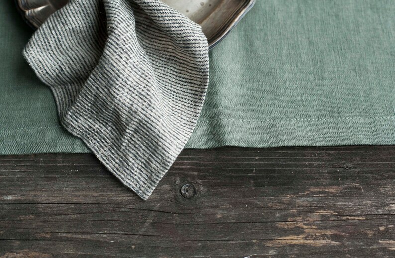 May include: A striped linen napkin folded on a green linen placemat and a wooden table.