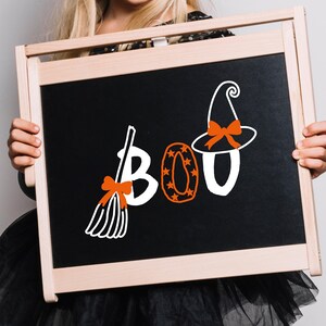 May include: A rectangular wooden chalkboard featuring the white and orange text BOO. The letter B is shaped like a broom with an orange bow, the letter O is orange with star patterns, and the second O is topped with a witch hat and orange bow.