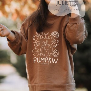 Op de afbeelding: Een bruin sweatshirt met lange mouwen en een witte grafische print van een pompoen, een eikel, een dennenappel, een regenboog en bladeren. De tekst luidt little PUMPKIN and friends. De afbeelding bevat een watermerk met de tekst JULIETTE pieces SVG DXF PNG.