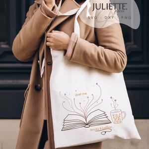 May include: A white canvas tote bag featuring a brown line art illustration of an open book with lines extending upward into small hearts, accompanied by a coffee mug and the text "Just Me" and "Books & Coffee" printed in a brown script font.