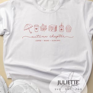 Puede incluir: Una camiseta blanca con un gráfico de líneas rojas que muestra un paraguas, una taza de café, una hoja de arce, una pila de libros con la etiqueta "BOOK CLUB", una vela y un cupcake. Debajo de los iconos, el texto dice "autumn chapter" y "COFFEE • BOOKS • SLOW DAYS".