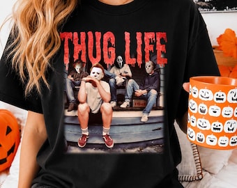 May include: A black t-shirt featuring the red text THUG LIFE above a graphic of four horror movie characters sitting on porch steps. The characters include figures wearing masks resembling Michael Myers, Ghostface, and Jason Voorhees.