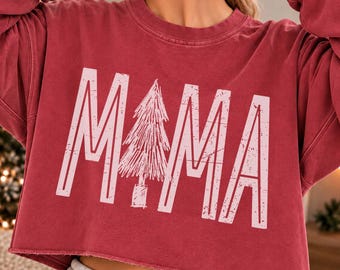 May include: A dark red long-sleeve cropped sweatshirt with a raw hem. The front features the text MAMA in large, light pink, distressed-style block letters, with a sketch-style pine tree replacing the letter A.
