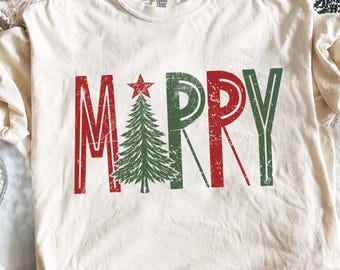 May include: A cream-colored short-sleeve t-shirt featuring the text MERRY in a distressed font. The letter E is replaced by a green pine tree topped with a red star. The letters M and R are red, while the letters R and Y are green.