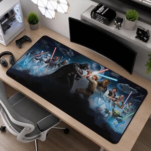 Puede incluir: Una alfombrilla de escritorio rectangular con un estampado gráfico de Star Wars. El diseño muestra varios personajes, incluidos Darth Vader, Luke Skywalker, Yoda y soldados de asalto, en una batalla con sables de luz sobre un fondo espacial oscuro.