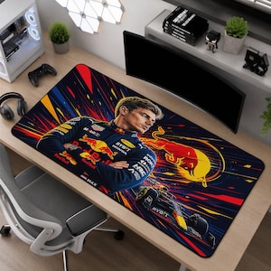 Puede incluir: Una alfombrilla de escritorio rectangular con una ilustración gráfica de un piloto de Fórmula 1 con traje de carreras azul marino con la marca Red Bull, brazos cruzados, junto a un logotipo de toro amarillo y un coche de carreras.