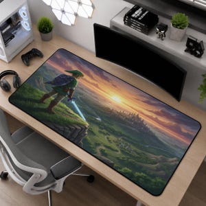 May include: A rectangular desk mat featuring a printed illustration of a character in a green tunic standing on a grassy cliff edge, holding a glowing sword, overlooking a sprawling valley landscape with a distant castle at sunset.