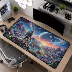 May include: A rectangular desk mat featuring a vibrant, colourful space-themed illustration of an astronaut standing on a rocky alien planet surface, with a large ringed planet, distant stars, glowing flora, and a spacecraft in the background.