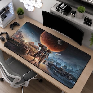 Puede incluir: Una alfombrilla de escritorio rectangular con un paisaje de ciencia ficción que muestra a dos figuras sobre un terreno rocoso bajo un gran planeta naranja y una luna pequeña. La escena incluye un vehículo futurista, montañas y cielo estrellado.