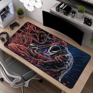 May include: A rectangular desk mat featuring a detailed graphic illustration of the characters Venom and Carnage in a dynamic confrontation. The design showcases Venom in black and Carnage in red, both with sharp teeth and long tongues.