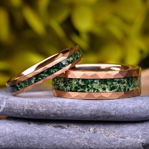 Pode incluir: Dois anéis de ouro rosa com exterior facetado e incrustação central de ágata musgo verde. Os anéis apresentam um acabamento metálico polido nas bordas e uma incrustação de pedra verde texturizada e salpicada no centro de cada banda.