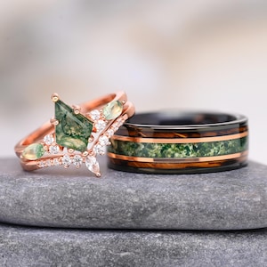 Op de afbeelding: Een roségouden ring met een vliegervormige mosagaat middensteen, kleine heldere accentstenen en twee zijdelingse mosagaat cabochons, gecombineerd met een zwarte ring met een centrale mosagaat inleg en roségouden strepen.