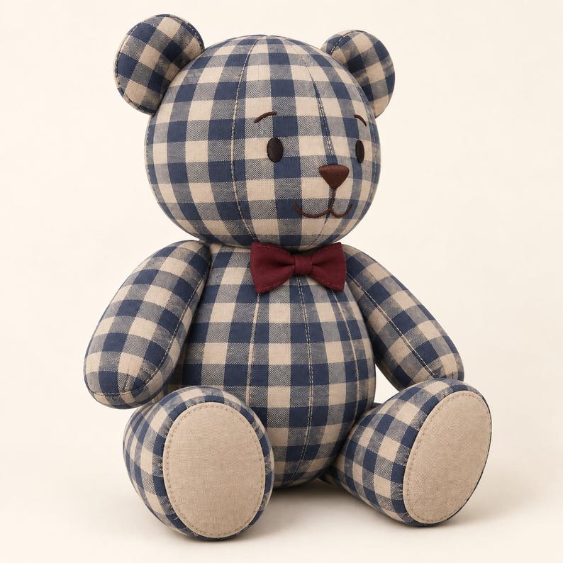 Puede incluir: Un oso de peluche con un patr&oacute;n de cuadros vichy en azul y beige por todo el cuerpo. El oso tiene orejas redondas, una nariz y boca cosidas en marr&oacute;n oscuro, y una pajarita de color granate oscuro liso sujeta al cuello. Las plantas son beige.