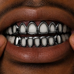 Peut inclure: Un ensemble de grillz couleur bronze à canon poli recouvrant les dents supérieures et inférieures. Les cadres métalliques présentent des découpes individuelles pour chaque dent, créant une bordure réfléchissante autour de l'émail blanc.