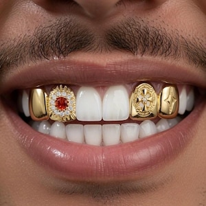 Peut inclure: Un ensemble de grilles dentaires en or portées sur les dents supérieures. Le design comprend deux coiffes en or uni, une coiffe avec une pierre rouge centrale entourée de petites pierres claires, une avec une croix gravée et une avec une étoile.