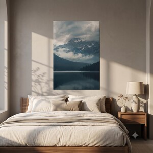 May include: A vertical wall art print featuring a dark, moody landscape of a mountain range partially obscured by low-hanging clouds, with a calm, reflective lake in the foreground and a dense forest line along the shore in deep blue and grey tones.