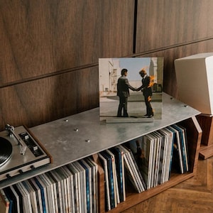 May include: A wooden record storage console with a metal top surface holding a turntable with a black vinyl record, a Pink Floyd Wish You Were Here album cover, and a white speaker. The console contains rows of vinyl records in sleeves.