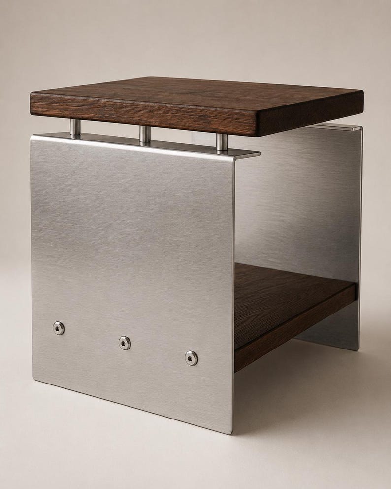 Op de afbeelding: Een bijzettafel met een donkerbruin houten blad en een onderste houten plank, ondersteund door twee zijpanelen van geborsteld zilverkleurig metaal. Het blad is met drie cilindrische afstandhouders aan het frame bevestigd en vastgezet met bouten.