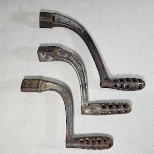 May include: Three antique cast iron stove door handles with intricate designs. The handles are in various shades of brown and gray with rust spots. The handle on the top has the word "ROBBINS" embossed on it.
