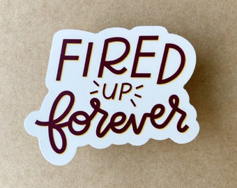 May include: White sticker with the text "FIRED UP forever" in a maroon and yellow script font.