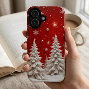 May include: A smartphone case featuring a vibrant red background with a winter scene of white snow-covered pine trees. The design includes scattered white snowflakes and small, metallic-looking spheres that resemble falling snow or ornaments.