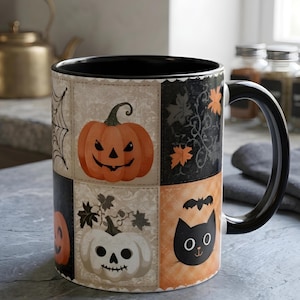 May include: A ceramic mug with a black interior and handle, featuring a grid pattern of Halloween-themed illustrations including an orange jack-o'-lantern, a white skull-shaped pumpkin, a black cat face, a spider web, and autumn leaves.