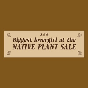 May include: A rectangular beige sign with dark brown text that reads Biggest lovergirl at the NATIVE PLANT SALE. The design features three small flower icons centered above the text and decorative scrollwork patterns in each of the four corners.