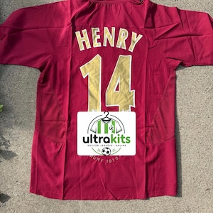 May include: A maroon short-sleeved soccer jersey with a collar, featuring the name HENRY and the number 14 in gold lettering on the back. A white rectangular label with the text ultrakits SOCCER JERSEYS ONLINE and a soccer ball icon is centered.