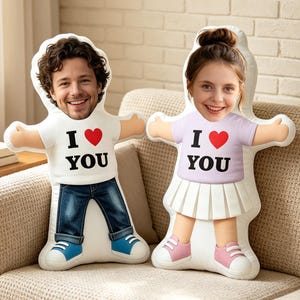 Puede incluir: Dos cojines de peluche con formas personalizadas y rostros fotográficos. Uno muestra a una persona con una camiseta blanca con el texto I heart YOU y vaqueros azules. El otro muestra a una persona con una camiseta morada clara con I heart YOU y una falda blanca.