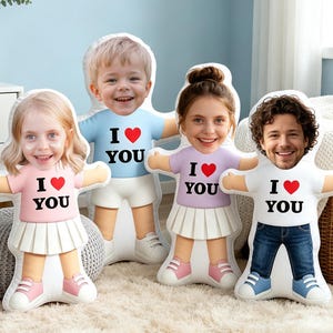 May include: Four custom-shaped plush pillows featuring photographic faces of children and an adult. Each pillow depicts a person wearing a shirt with the text I heart YOU, paired with skirts or pants, and sneakers, creating a set of personalized dolls.