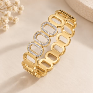 May include: A gold-toned bracelet featuring a series of interconnected oval links. Several of the oval links are embellished with small, clear, sparkling stones set along their surfaces, while the remaining links are plain polished gold-toned metal.
