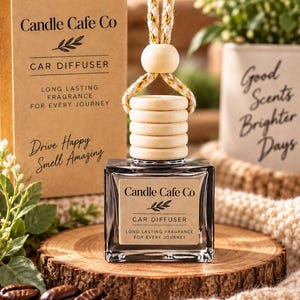 May include: A square glass car diffuser bottle with a light brown label reading Candle Cafe Co, Car Diffuser, Long Lasting Fragrance For Every Journey, Drive Happy Smell Amazing. It has a wooden cap, a hanging cord, and a matching cardboard box.