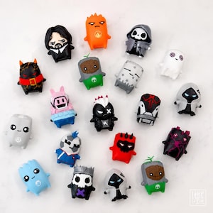May include: A collection of nineteen small, stylised vinyl character figurines featuring diverse designs, including figures resembling a bearded man, a ghost, a skull, a tree-like creature, and various masked or hooded beings in vibrant colours.