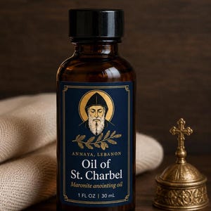 May include: An amber glass bottle with a black cap featuring a blue label with gold accents. The label displays an illustration of a bearded figure in a hood, the text Annaya, Lebanon, Oil of St. Charbel, Maronite anointing oil, and 1 FL OZ | 30 mL.