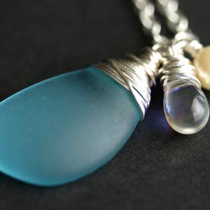 K&ouml;nnte beinhalten: Eine silberne Kettenkette mit einem blauen Glasanh&auml;nger, einer klaren, schillernden Glasperle und einer wei&szlig;en Perle.