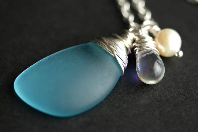 K&ouml;nnte beinhalten: Eine silberne Kettenkette mit einem blauen Glasanh&auml;nger, einer klaren, schillernden Glasperle und einer wei&szlig;en Perle.