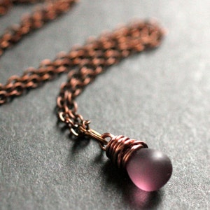 May include: A copper chain necklace with a purple glass pendant wrapped in copper wire.
