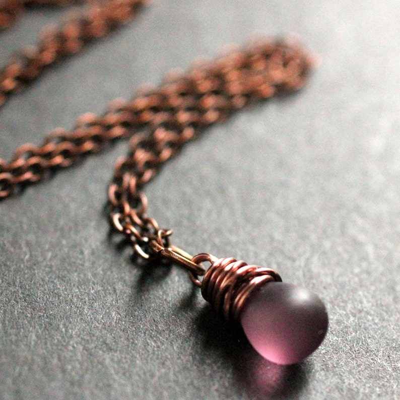 May include: A copper chain necklace with a purple glass pendant wrapped in copper wire.