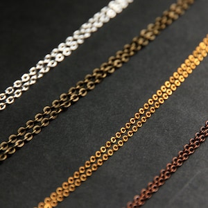 May include: Four different chain styles in silver, bronze, gold, and copper. The chains are laid out in parallel lines on a black background.
