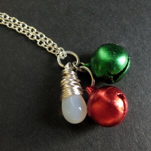 Puede incluir: Un collar de cadena de plata con tres colgantes: un colgante blanco en forma de l&aacute;grima, un colgante de campana verde y un colgante de campana roja.