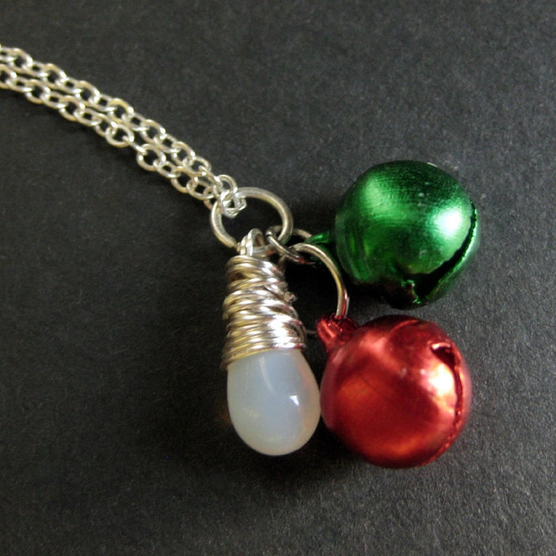 Puede incluir: Un collar de cadena de plata con tres colgantes: un colgante blanco en forma de l&aacute;grima, un colgante de campana verde y un colgante de campana roja.