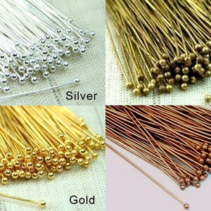 K&ouml;nnte beinhalten: Sortiment von Stiften mit Kopf in vier verschiedenen Farben: Silber, Gold, Bronze und Kupfer. Jeder Stift hat einen kleinen runden Kopf.