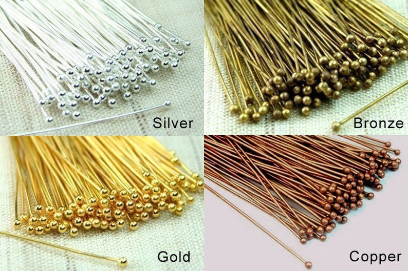 K&ouml;nnte beinhalten: Sortiment von Stiften mit Kopf in vier verschiedenen Farben: Silber, Gold, Bronze und Kupfer. Jeder Stift hat einen kleinen runden Kopf.