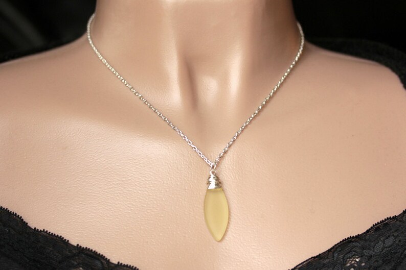 May include: A silver chain necklace with a light yellow teardrop-shaped pendant.