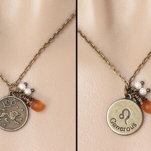 Op de afbeelding: Een bronzen ketting met een ronde hanger met het sterrenbeeld Leeuw en het woord "Leo". Het bevat een oranje kraal, witte parels en een bronzen ketting. De ketting wordt getoond tegen een neutrale achtergrond.