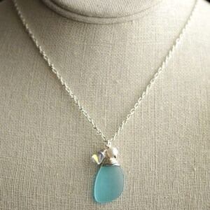 K&ouml;nnte beinhalten: Eine silberne Kettenkette mit einem hellblauen Meerglass Anh&auml;nger und einem kleinen silbernen Anh&auml;nger.