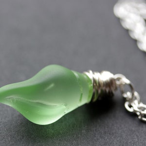 May include: A silver chain necklace with a green glass pendant shaped like a teardrop. The pendant is frosted and has a subtle swirl design.
