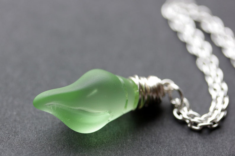 May include: A silver chain necklace with a green glass pendant shaped like a teardrop. The pendant is frosted and has a subtle swirl design.